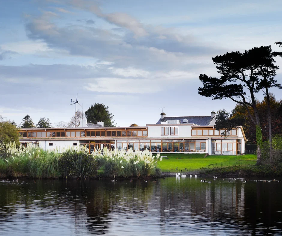 Photo of Castle Espie, water in foreground, building in the middle of the image and sky with clouds at the top, depicting overall haven for wildlife scene