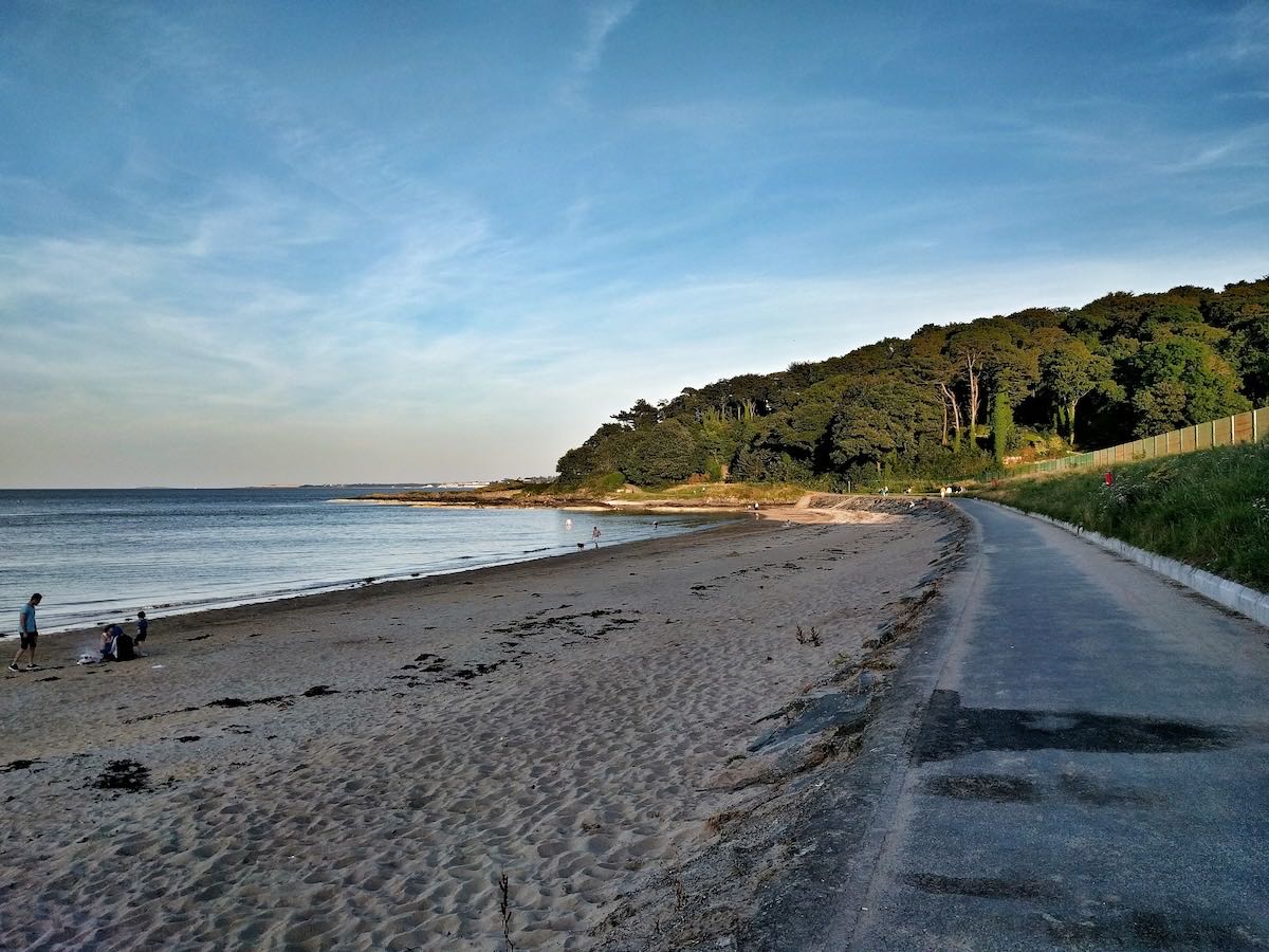 The sandy curve of Helen's Bay beach with a wooded headland behind
