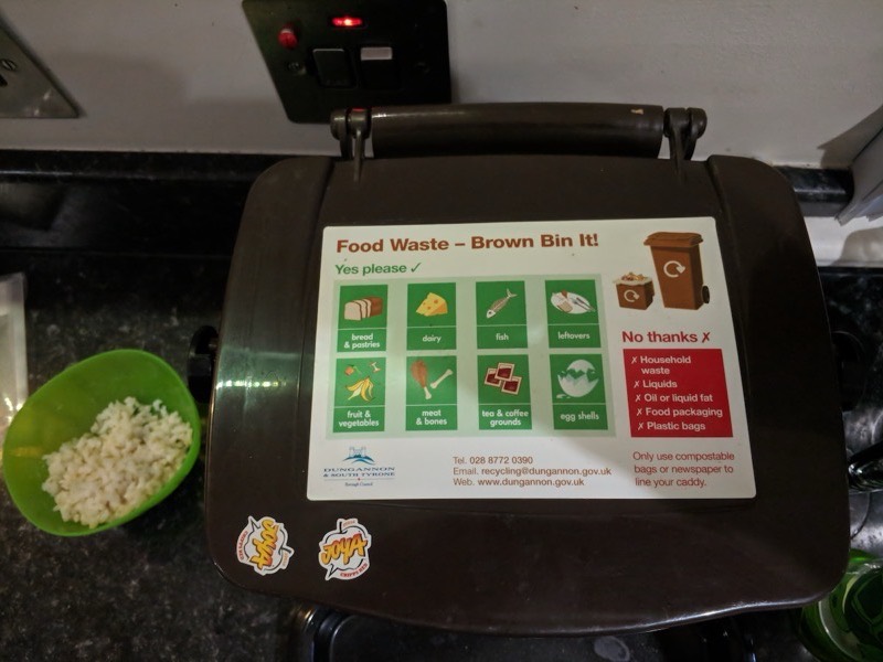 A kitchen food waste caddy with a council recycling guide on the lid