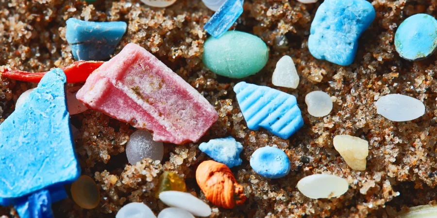 photo of colourful pieces on plastic on sand , including little round nurdles